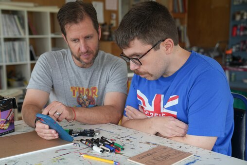 Eric Gordon, a staffer at Make Studio, shows Tony Labate some artistic references as Labate works on new pieces. Baltimore, Md. July 10, 2025.