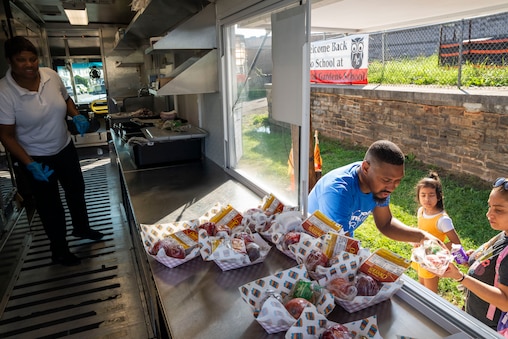 Employees Sabrina Burguss, left, and Billy Logan, right, serve food from the Streats Cafe food truck parked outside of Armistead Gardens Elementary/Middle School on July 3, 2025.