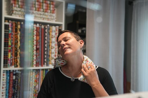 Claudia Phillips, the owner of Cherapy, demonstrates how to wear her product in her home in Columbia, Howard County, Md. on July 7, 2025. Phillips says that by heating up the pillow in the microwave, it can help customers relieve tension.