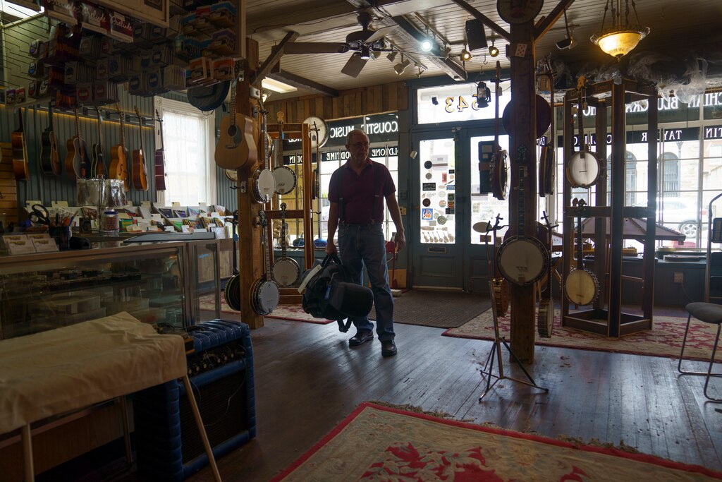 Bill Racine, a sales associate at the Appalachian Bluegrass Shoppe in Catonsville, Baltimore County, Md. holds a guitar on July 2, 2025.
