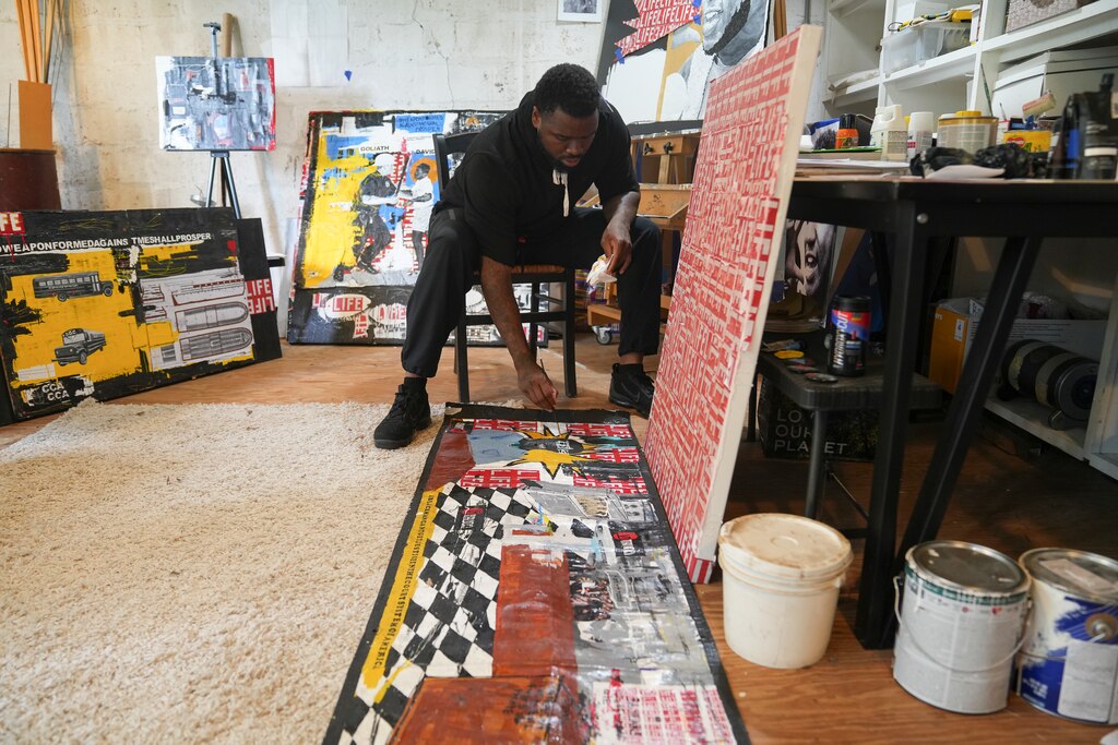 Waymond Harrison continues to rework his painting on June 17, 2025. He has been repairing this piece for fourteen years months now. The painting is a collage piece representing his life through incarceration and the American court system.