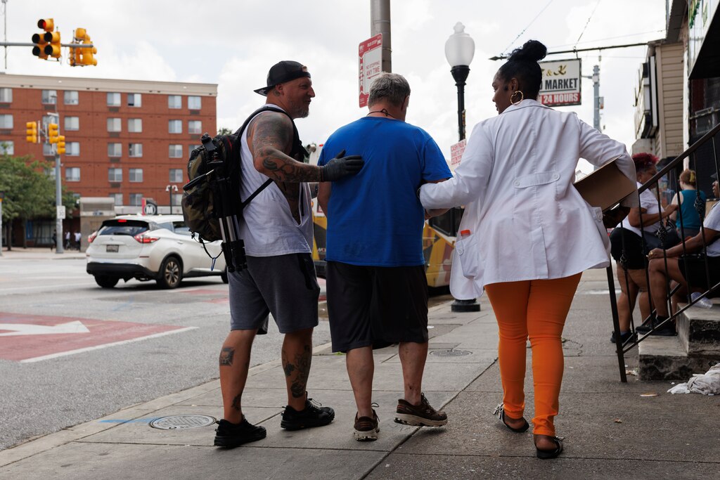 Community outreach members assist a man after he got assistance from emergency crews for an overdose at Penn North on Friday, July 11, 2025 in Baltimore. Just a day following a mass-overdose in the area.