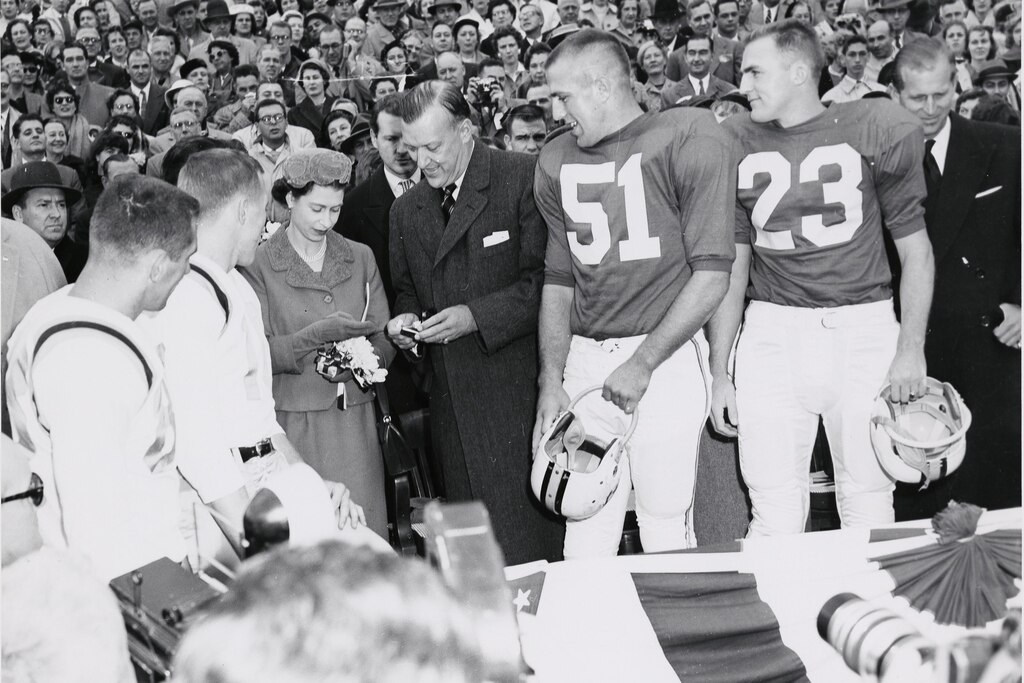Queen Elizabeth II with Governor Theodore McKeldin and team captains while checking the coin to be used for the coin toss at a University of Maryland football game against the University of North Carolina, October 19, 1957. Prince Philip is pictured at the far right. Courtesy of University of Maryland Archives.