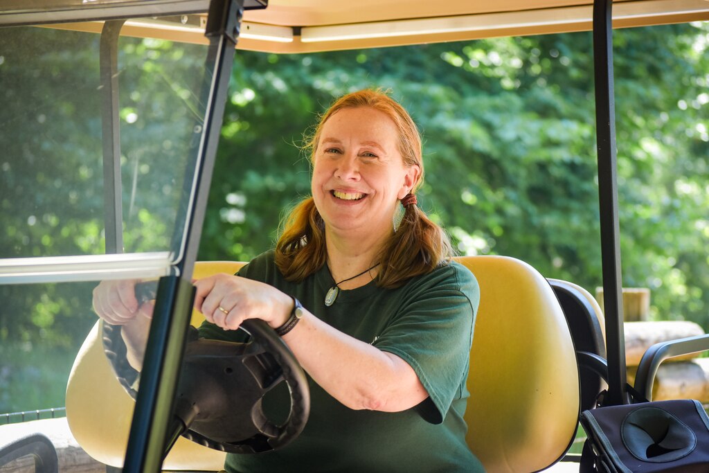 Margaret Innes, a woman with red hair in two ponytails, sits in a golf cart. She is wearing a green t-shirt.
