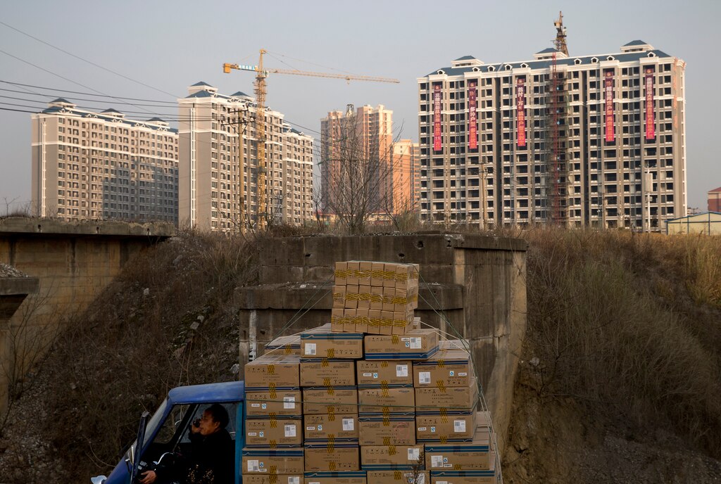 FILE - In this Monday, Jan. 20, 2014, file photo, a man talks on a mobile phone inside his tricycle cart loaded with goods near residential buildings under construction in Changsha, in China's Hunan province. Economists fear a lending bubble in China could threaten the global economy unless the Chinese government shores up its financial system, according to an Associated Press survey.