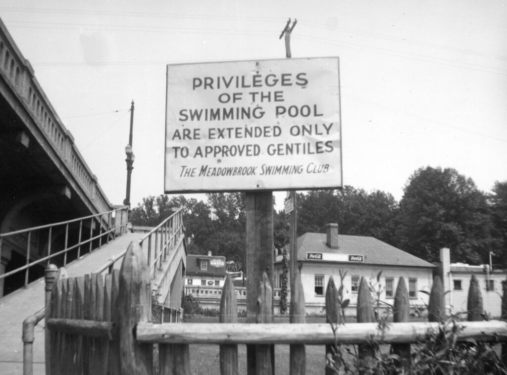 Black and white photograph of a sign outside of the Meadowbrook Swimming Club. The sign reads: "Privileges of the Swimming Pool Are Extended Only to Approved Gentiles The Meadowbrook Swimming Club." The photograph shows the walkway up to the pool as well as what is presumably the clubhouse in the background.
This sign was posted outside Meadowbrook, a privately owned swimming club in Baltimore City; though the photo is undated, and the issue of club restrictions persisted into the 1960s, we believe the image dates to 1942-1944, when the club's policy received a lot of pushback from the local Jewish (and others) community. The photo comes from a file of correspondence, photos, and other materials related to the push to have the policy changed, from the records of the Baltimore Jewish Council.