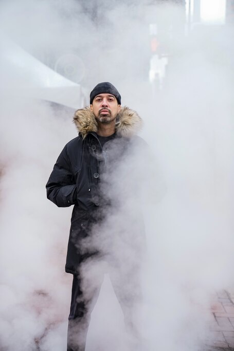 Man stands in black coat and poses for a photo.