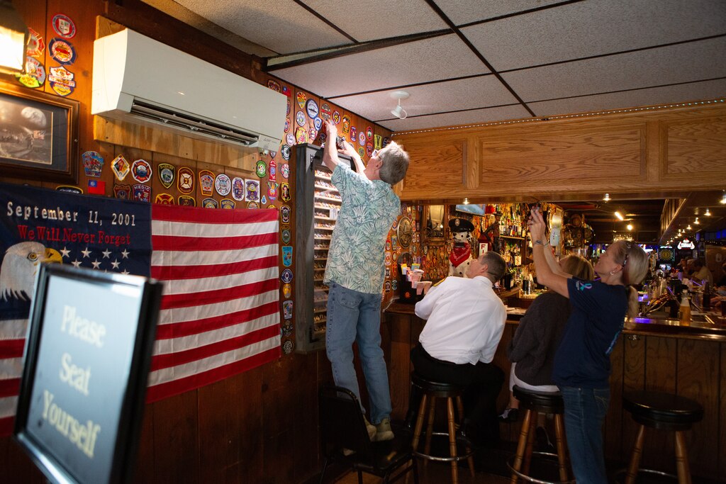 Bobby Ott, co-owner of the Ott House, staples new firefighter patches given to him by visiting firefighters to the wall of his pub. The collection of patches across the bar showcase the establishment's decades-long history of firefighter clientele. Ott estimates the academy drives 25-30% of his business.