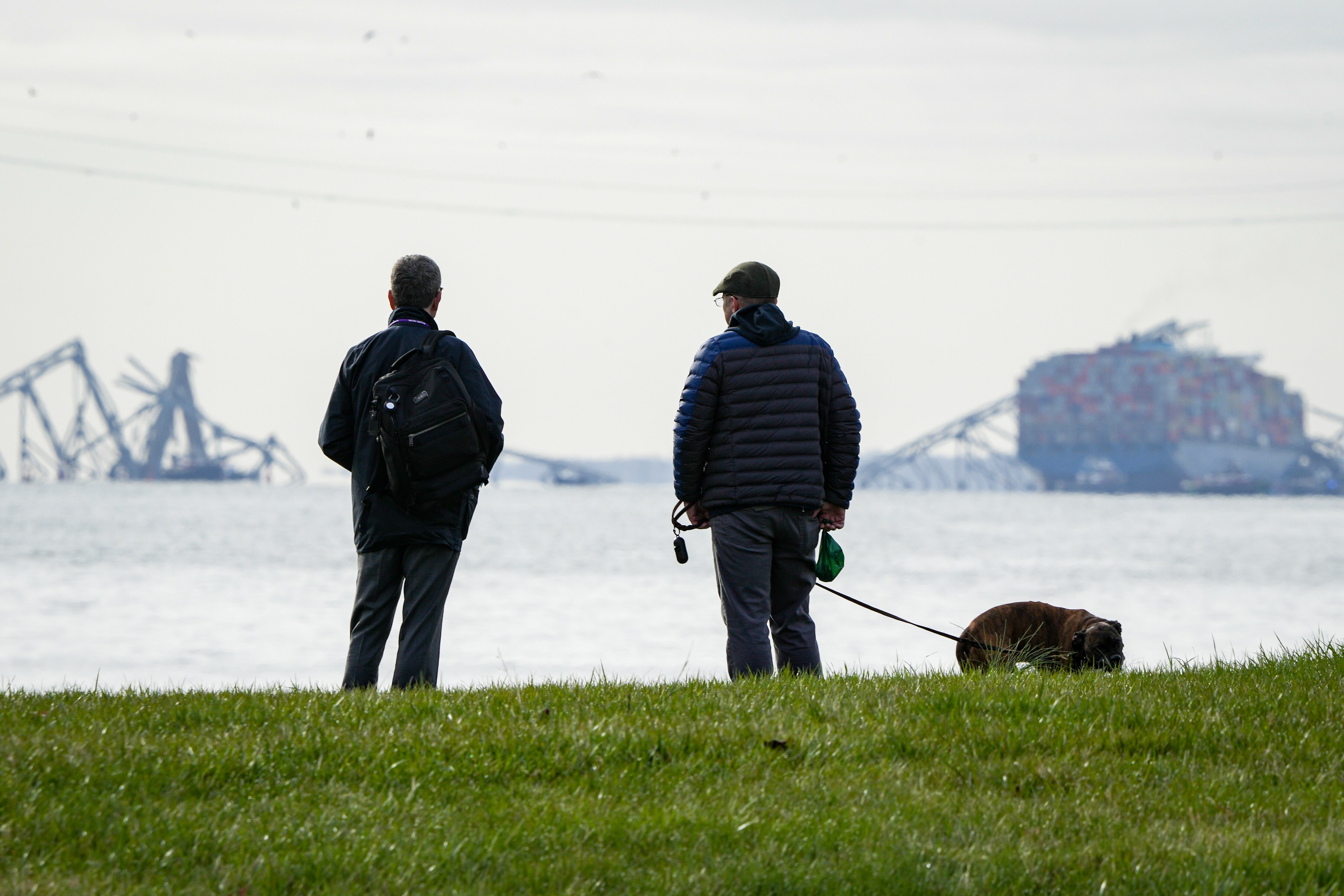 Two men observe the collapsed Francis Scott Key Bridge wreckage from Ft. McHenry on March 26, 2024. The bridge collapsed early Tuesday morning when a cargo ship collided with it.