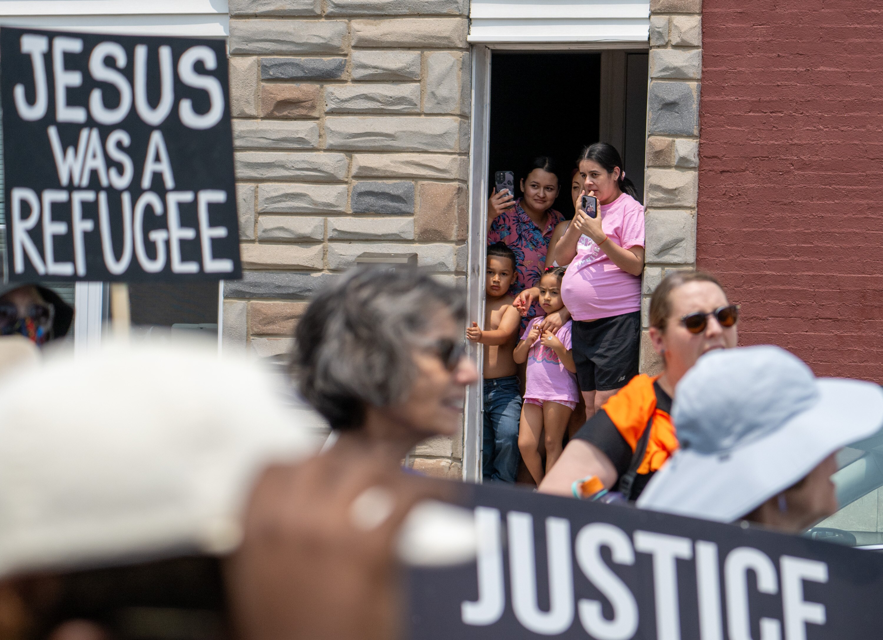 A family watches as protesters march through East Baltimore Wednesday afternoon in opposition to the intense immigration crackdown in Baltimore and around the country.