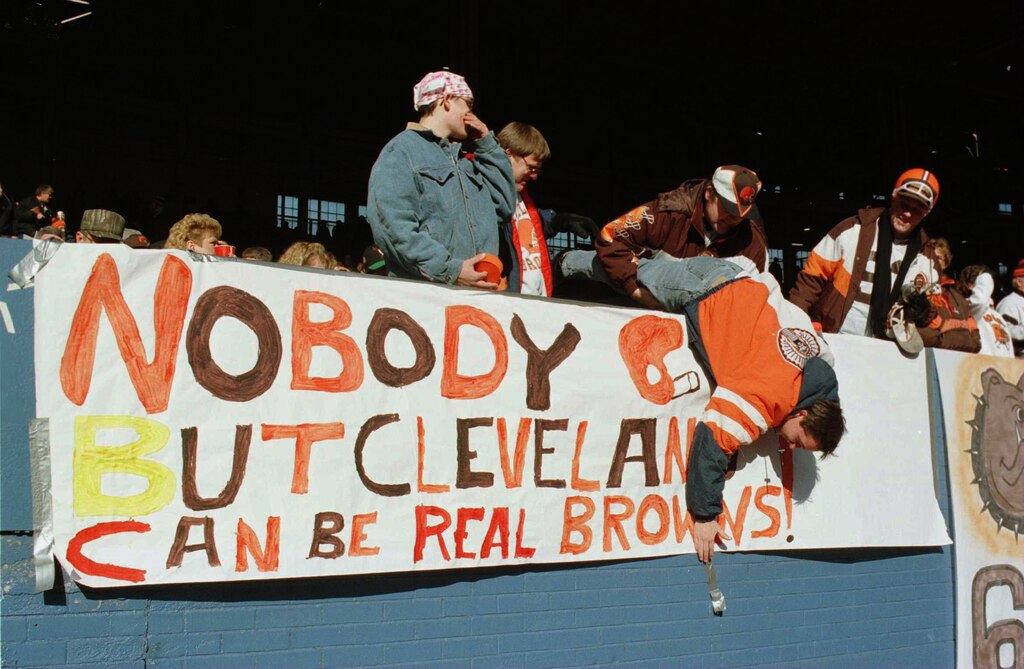 17 DEC 1995: Cleveland Browns fan Kenny Taylor is held by his father, Dwayne, while he posts a banner before the Cleveland v Cincinnati game at Cleveland stadium in Cleveland, Ohio. This was the Browns' last game in Cleveland before the team moved to Baltimore.
