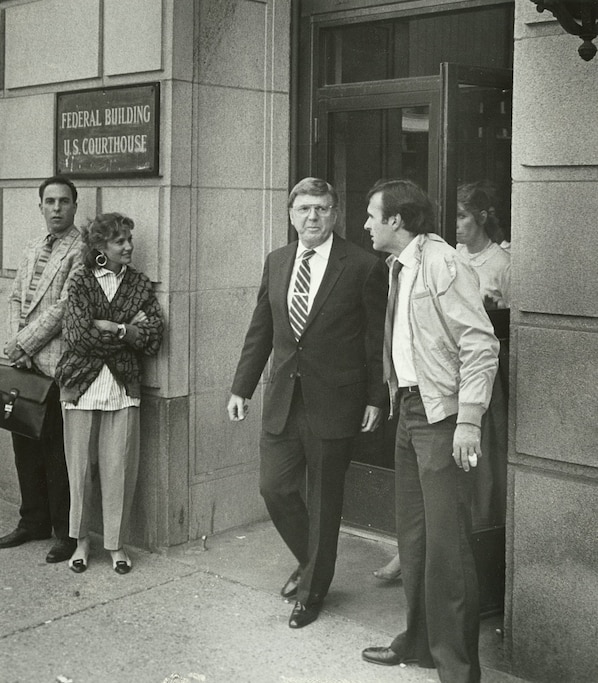 Black and white photograph of Carl Stevens exiting door of a federal courthouse, flanked by various people on left and right of the doors.