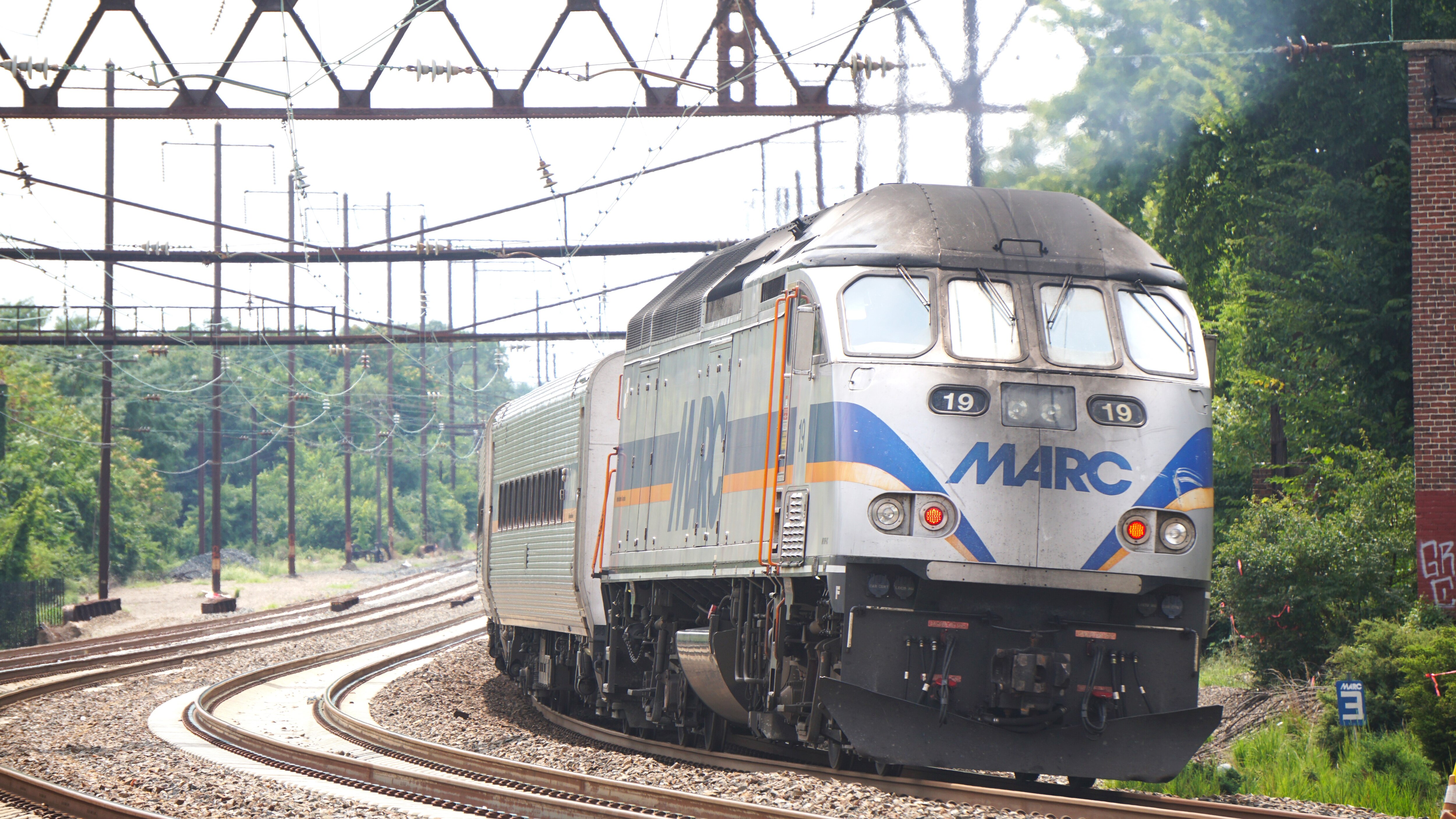A silver train that says "MARC" on the front rides down a train track.