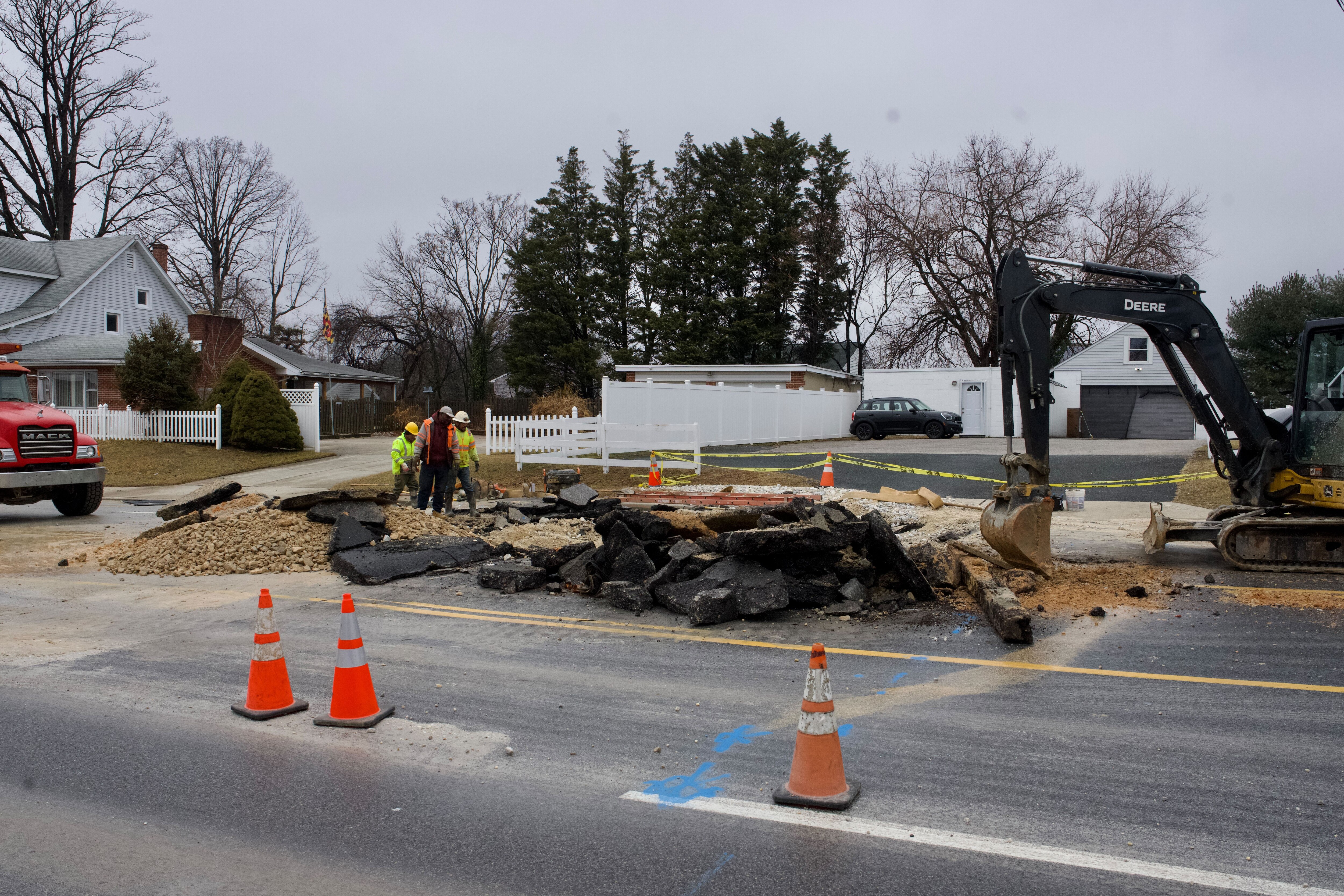 A small construction crew is seen at work near a large sinkhole on a divided highway. An excavator is to the right.