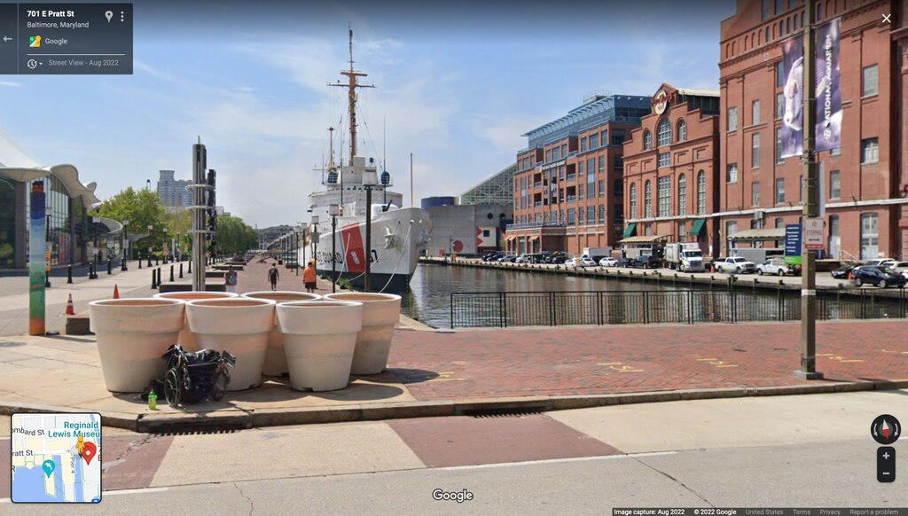 Google map screenshot of East Pratt Street showing unhoused man with wheelchair resting near flower pots before the "Baby Shark" speaker went up. Google image