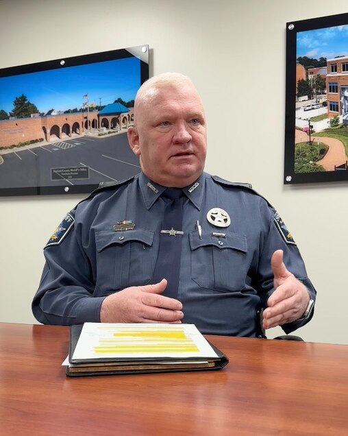 Photograph of man seated at table speaking. He wears the uniform of a staff member of Harford County Detention Center.