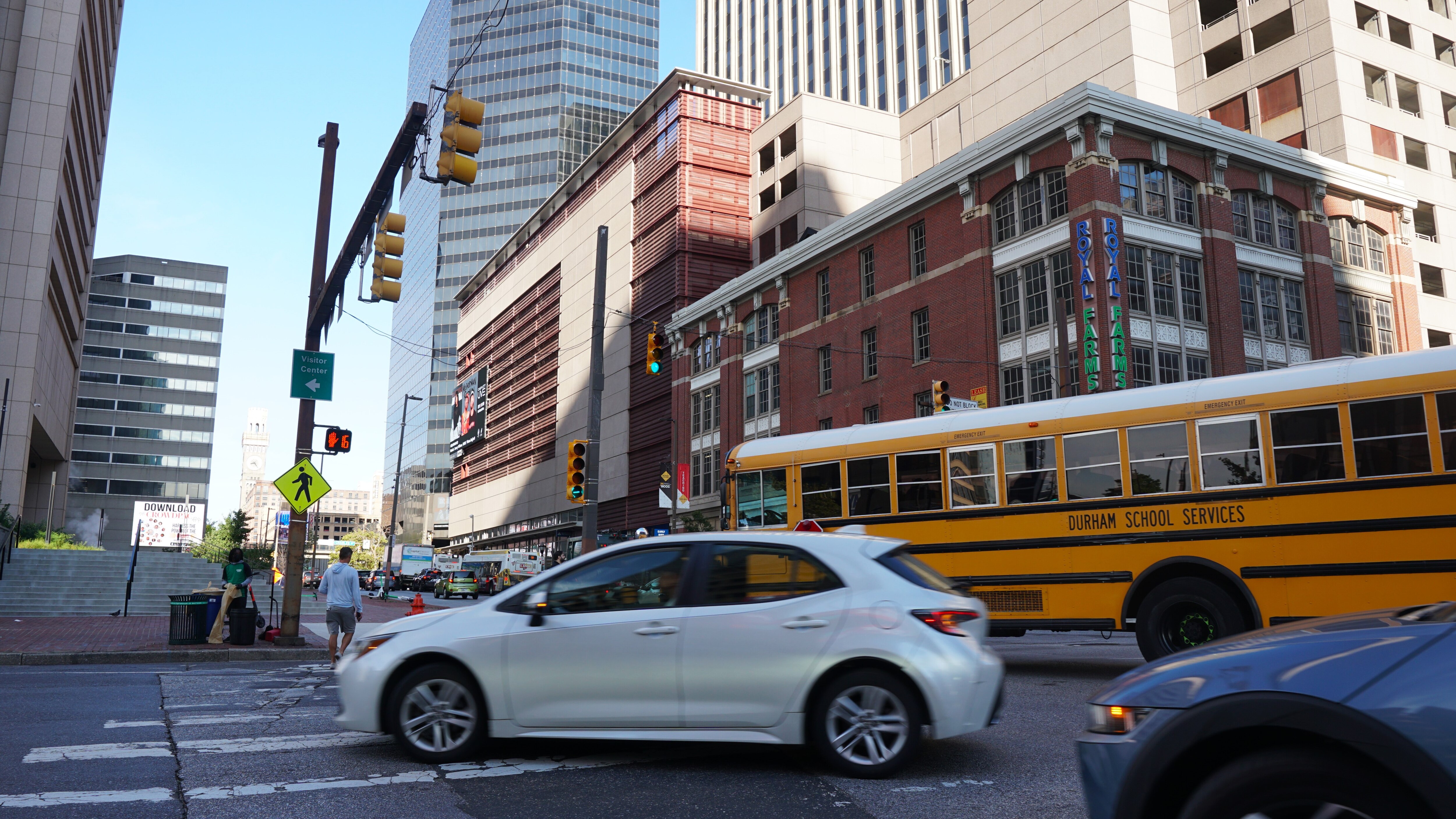 A white sedan and yellow school bus make a left turn on a busy city street.