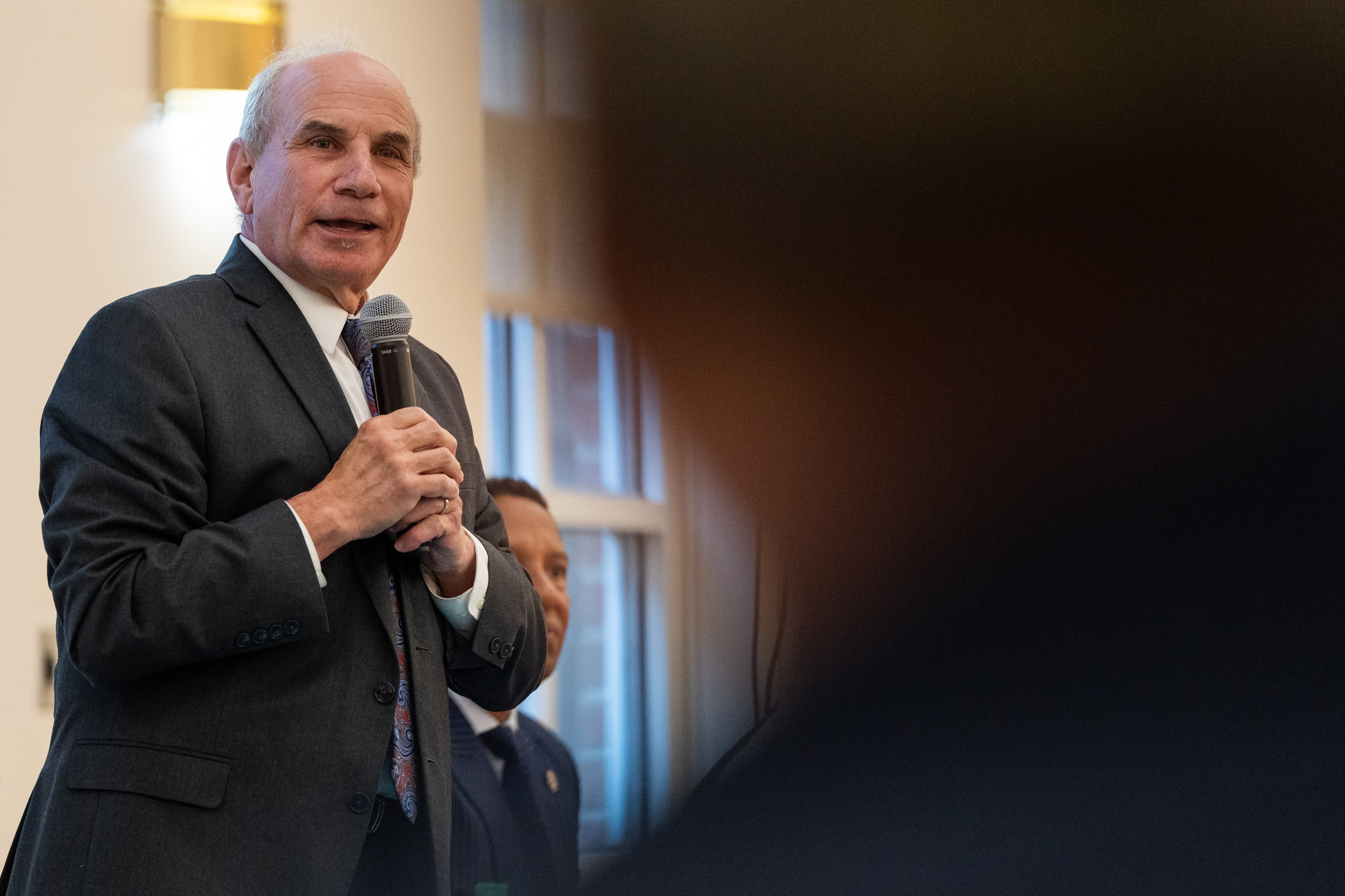 Israel “Izzy” Patoka speaks, framed to the left of a person’s shadowed and blurry head.