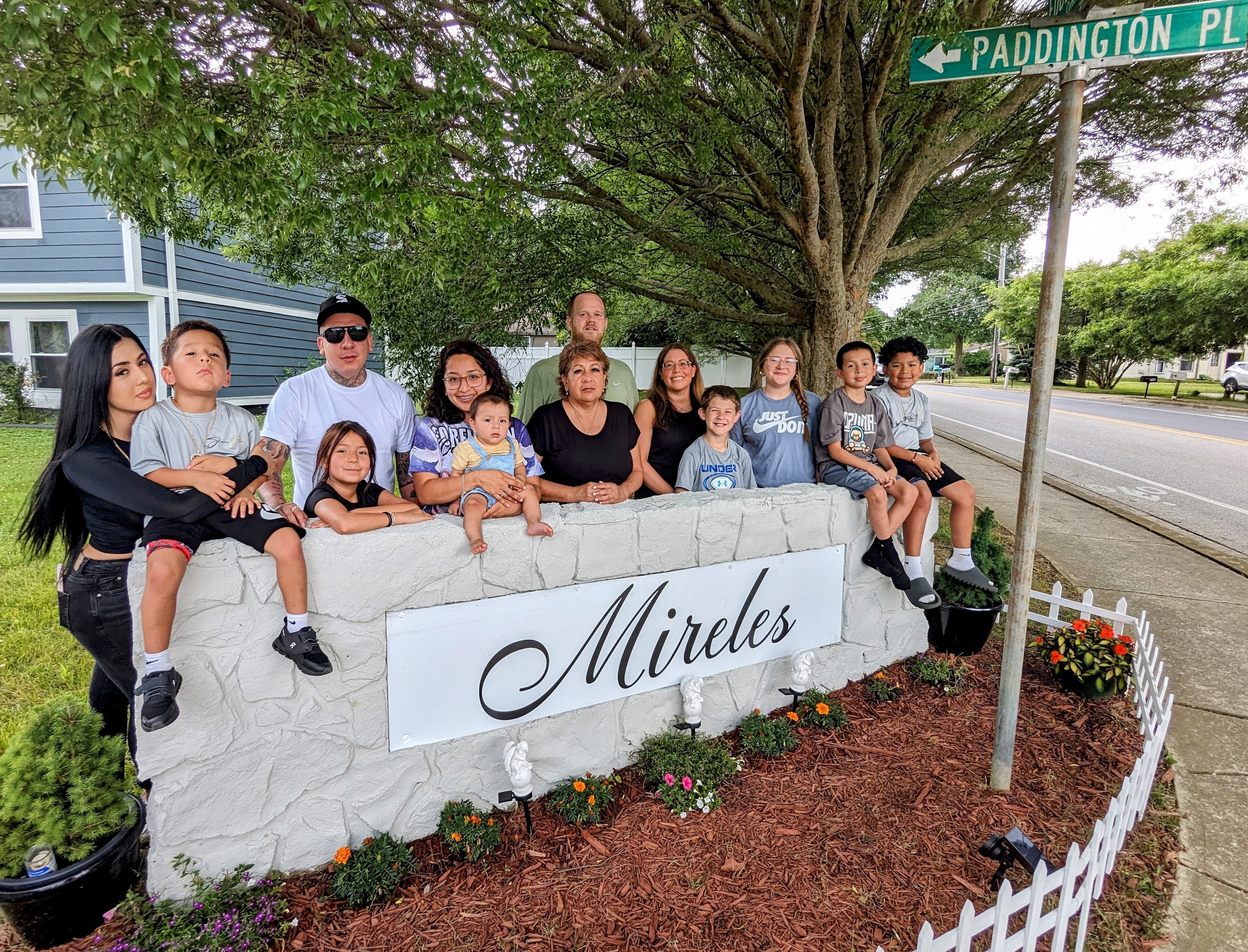Harcina Ruiz, center, stands with her family at the entrance sign to her neighborhood sign repainted to honor the memory of her son, Mario Mireles. Mario, his father Nicholas Mireles and their friend Christian Segovia were shot to death on the street on June 11, 2023.