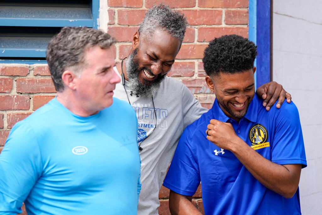 Football coach Dante Jones, center, laughs with Baltimore City Mayor Brandon Scott during a press conference outside Carver Vocational Technical High School during ‘Armour Day’ in Baltimore, Md., on Monday, Sept. 15, 2025.