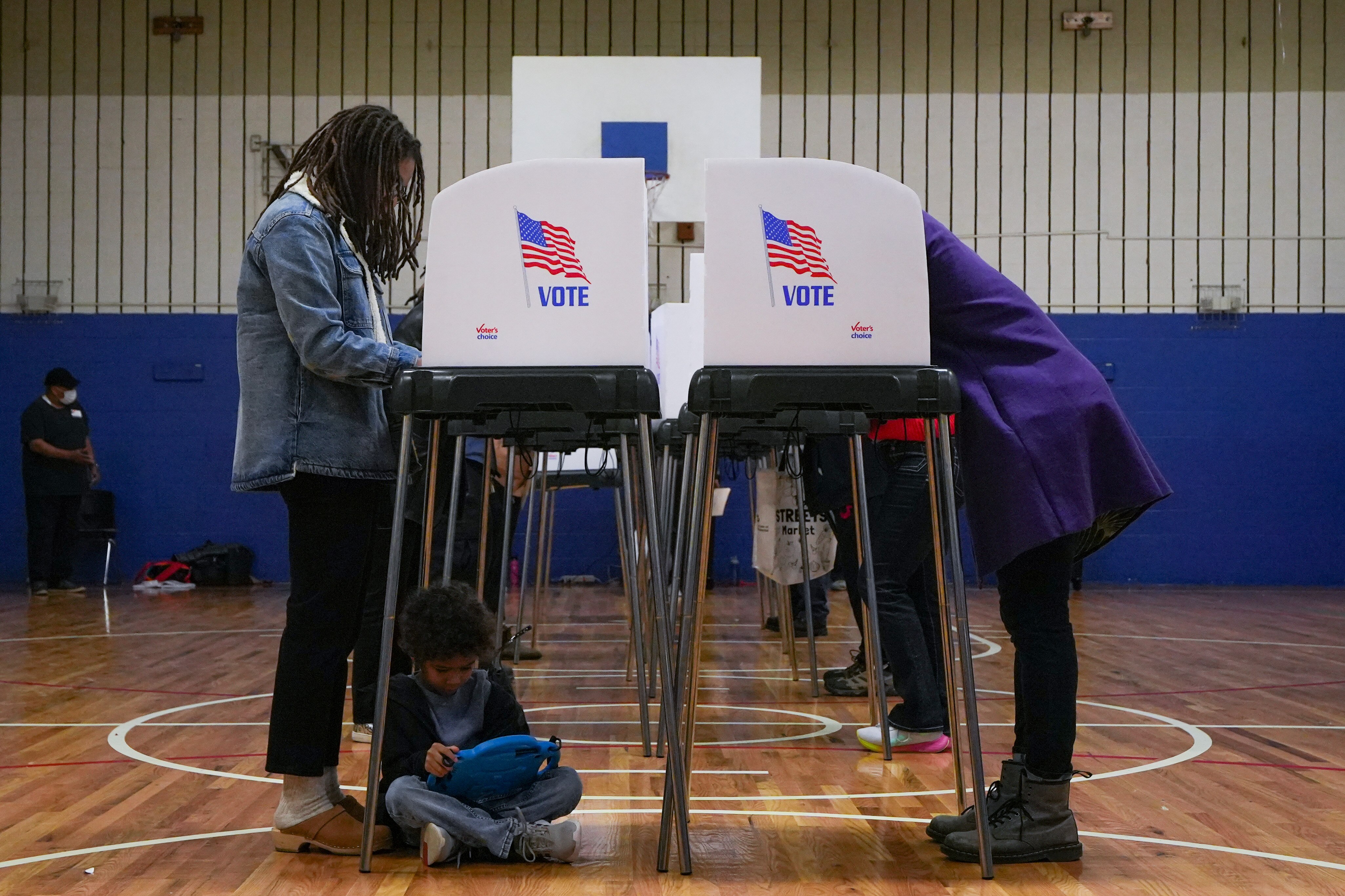 Keegan, 6, sits on the floor of Margaret Brent Elementary Middle School’s gymnasium as his mom, left, Katrina Washington, votes on Election Day, 11/8/22.