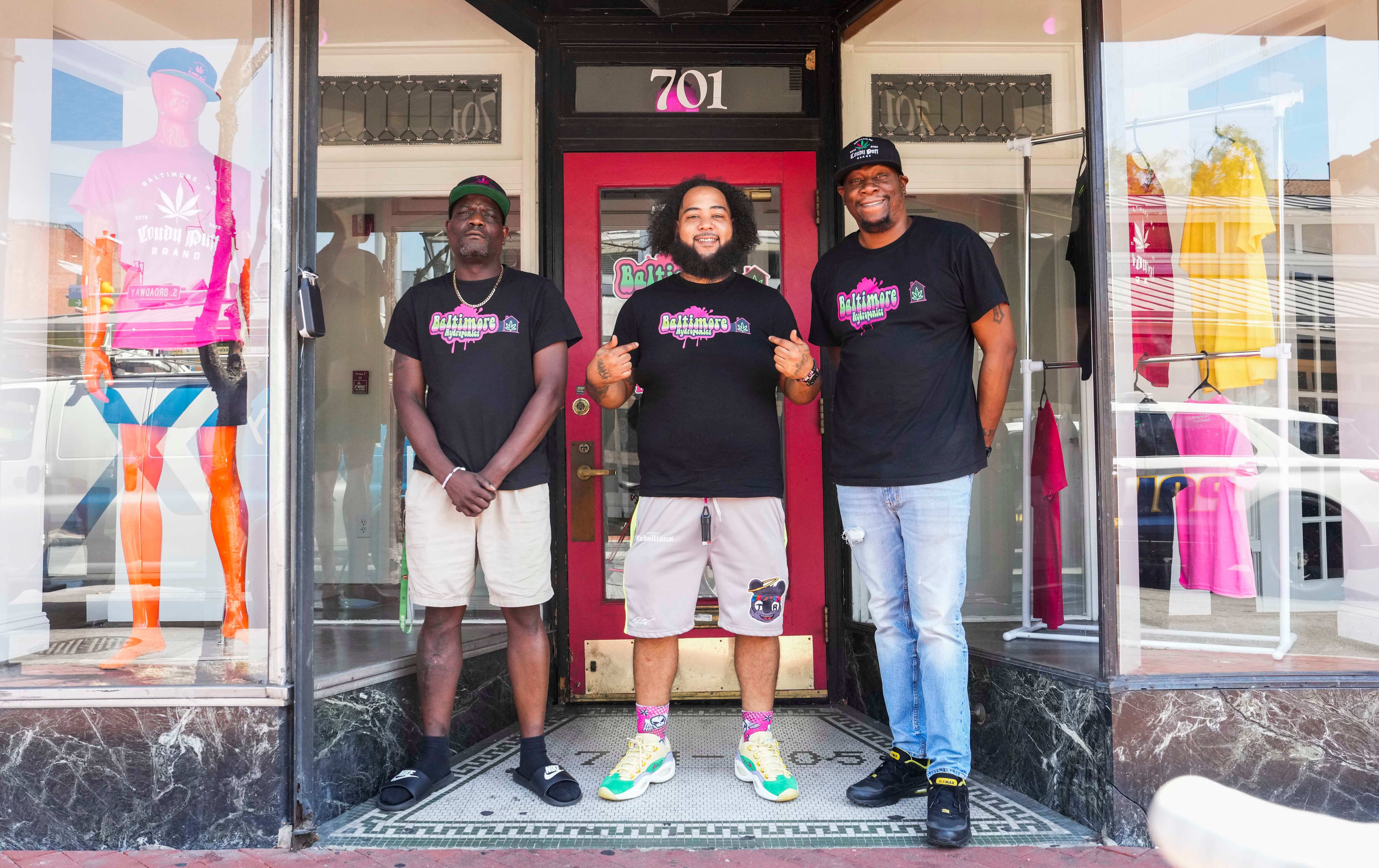 Three men wearing black t-shirts stand in front of the door to their Fells Point shop.