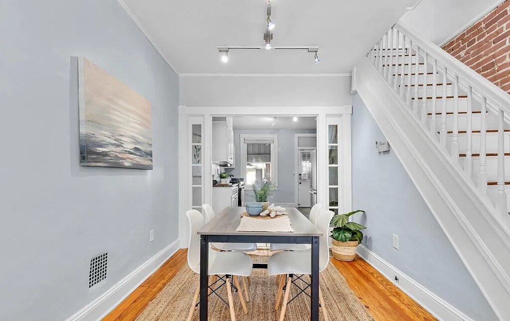 A dining room with light blue walls sits next to a white staircase.