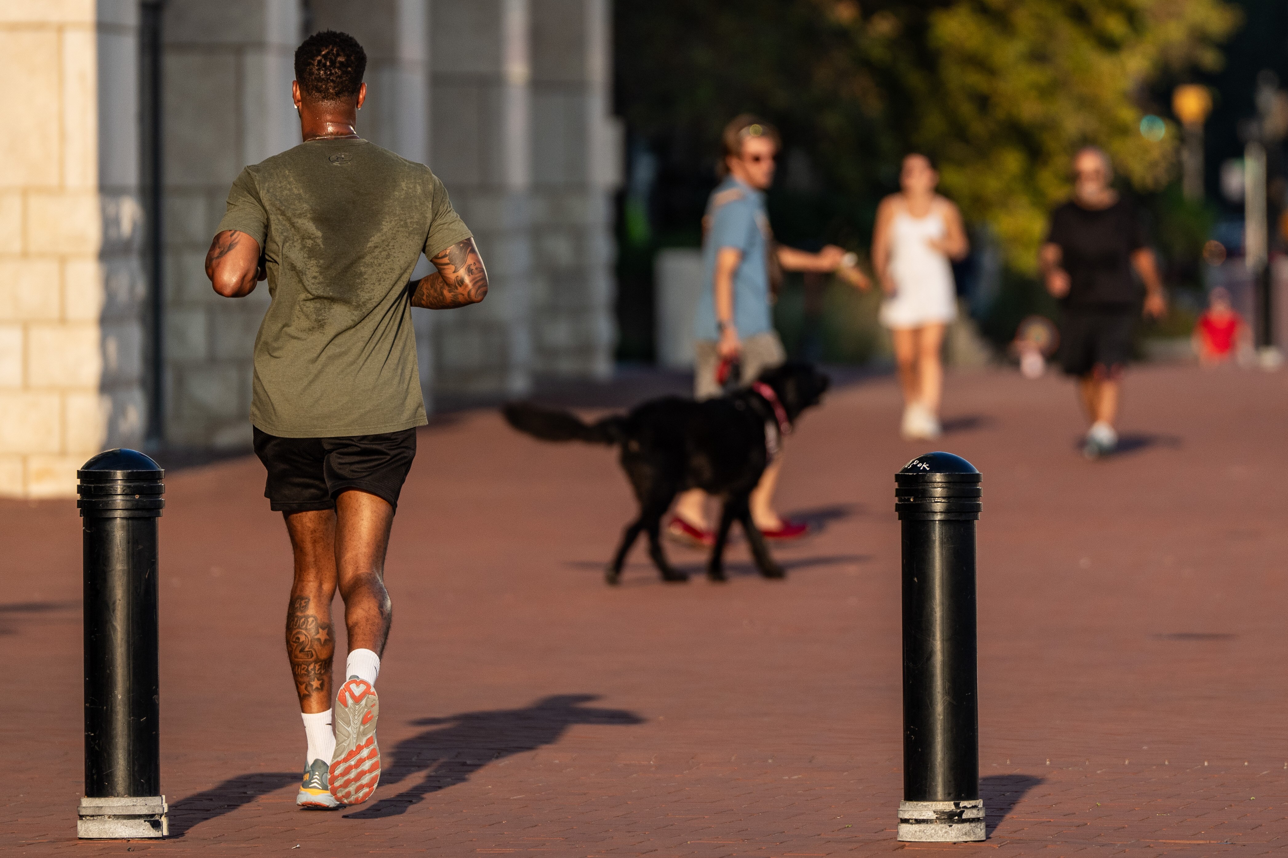 A man running away from the camera's t-shirt is drenched with sweat.