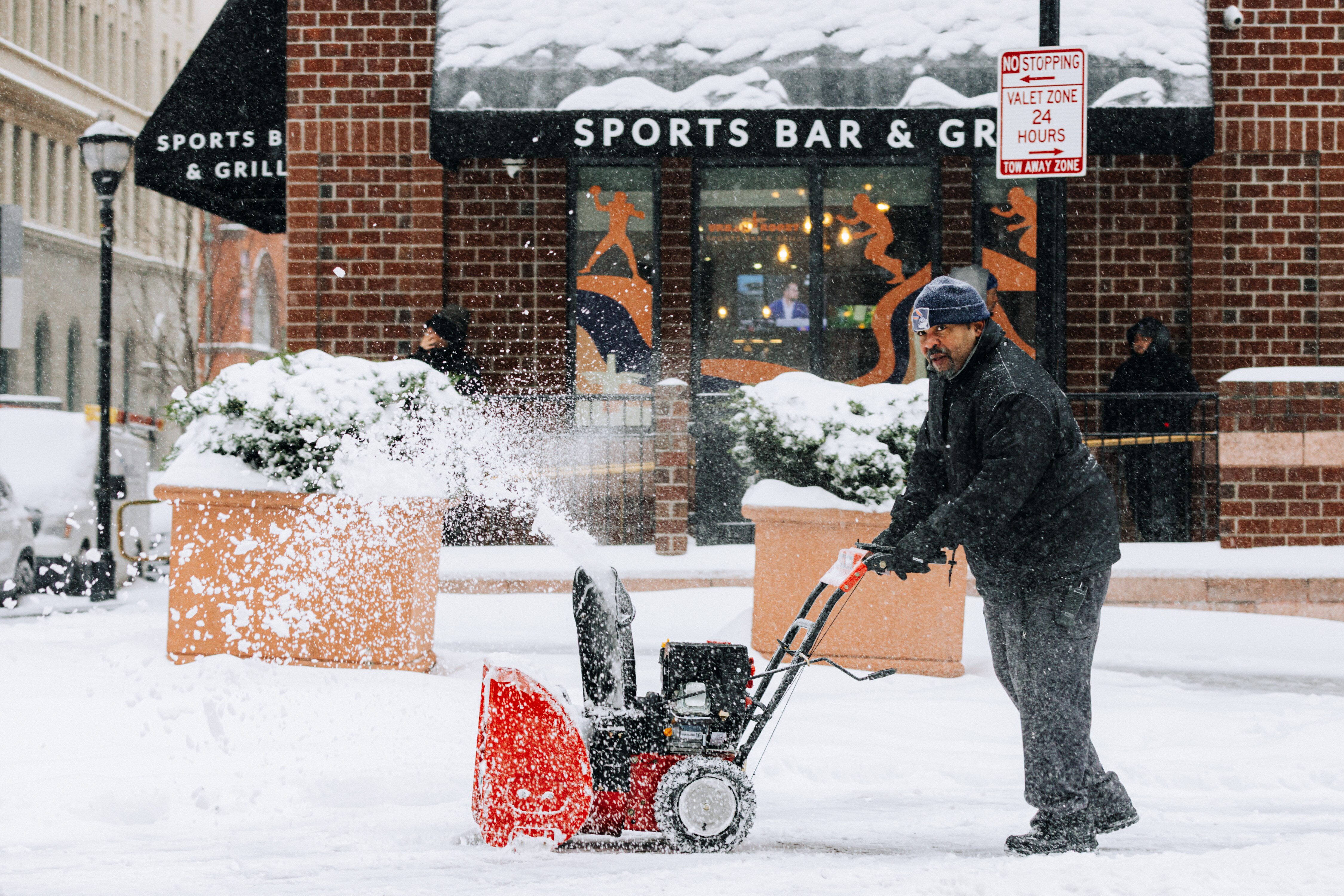 A man uses a snowblower in front of Urban Roost Sports Bar and Grill in Baltimore on Sunday.