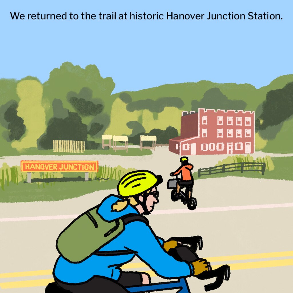 Illustration of two bicyclists on the road next to a historic red train station, with the trail in the background. A red sign next to the road in the middle ground says "Hanover Junction."