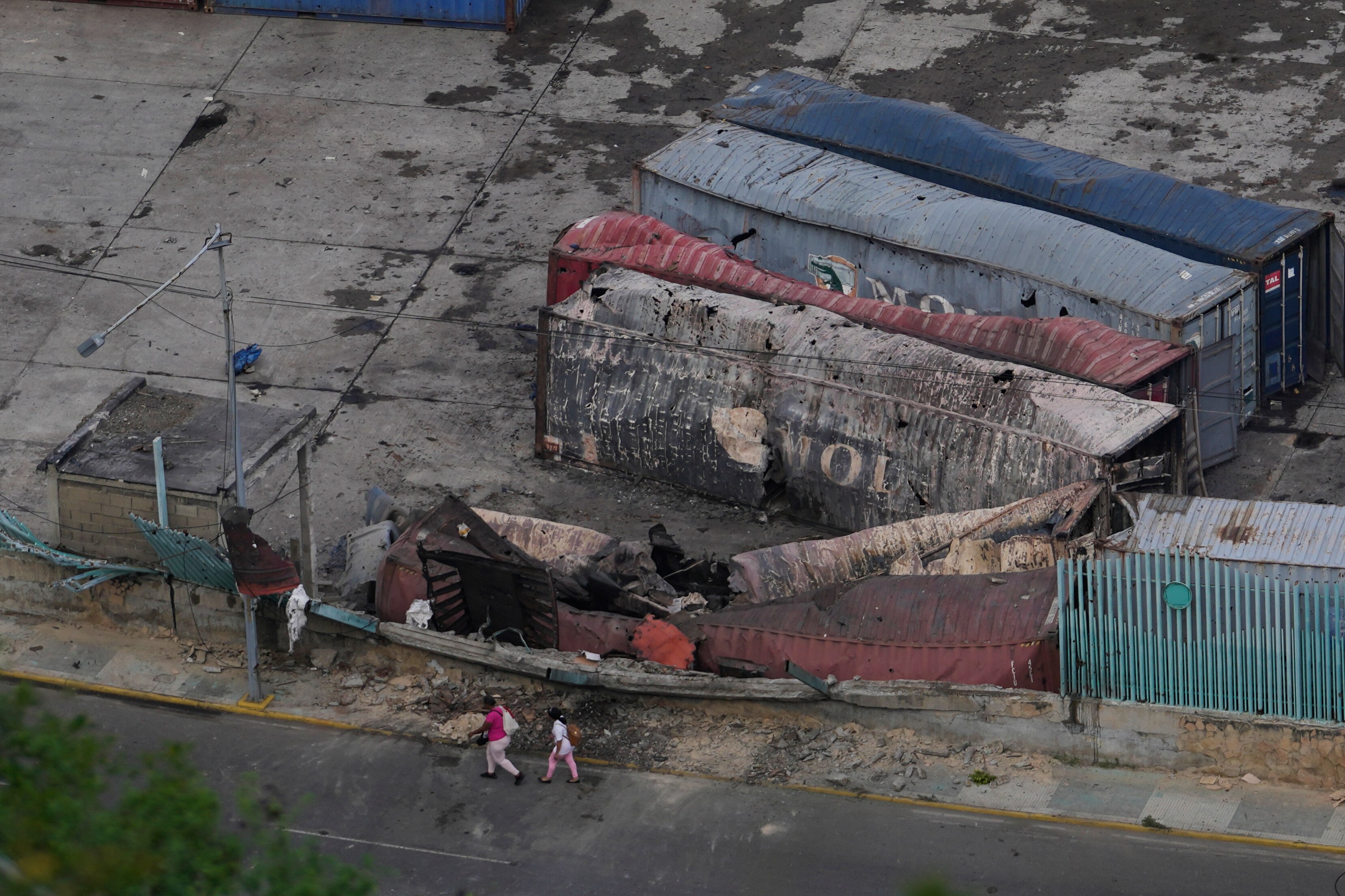 Pedestrians walk past destroyed containers at La Guaira port after explosions were heard in Venezuela, Saturday, Jan. 3, 2026.