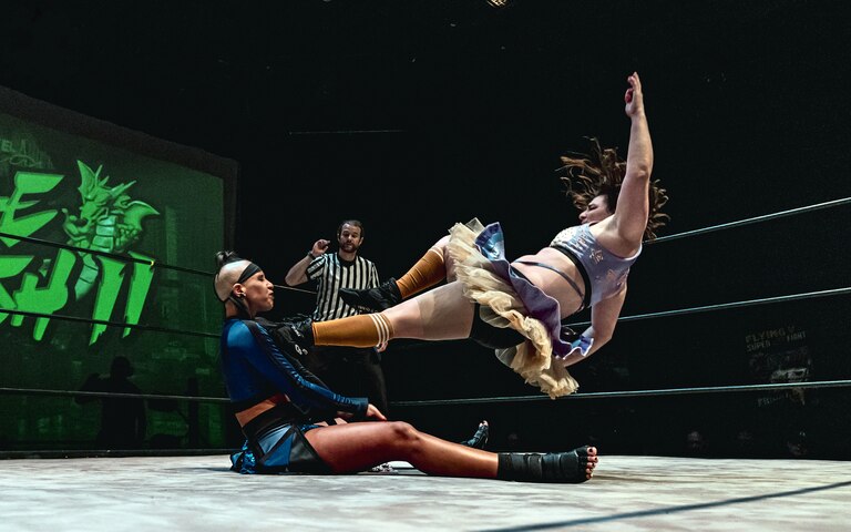 Abby Jane, right, dropkicks Janai Kai at Flying V Theatre's "Double Dash II" on May 31, 2025. Jane will wrestle in the main event of the nonprofit's "Fighter Fantasy" on Dec. 20 at Silver Spring Black Box Theatre.