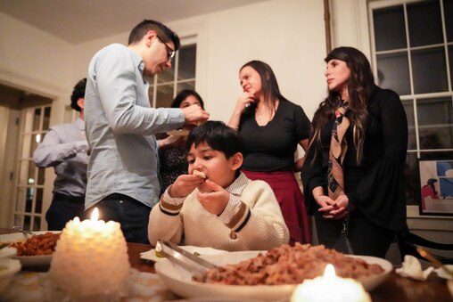 Nathaniel, 7, eats a taco, as pianist Joshua Espinoza speaks with other guests behind him following a Union Square Soirée in Baltimore, Md. on Friday, January 31, 2025. For a year now, a neighbor in Union Square has hosted intimate music concerts in his historic home’s salon to serve as a platform for newer artists and to share music with the community.