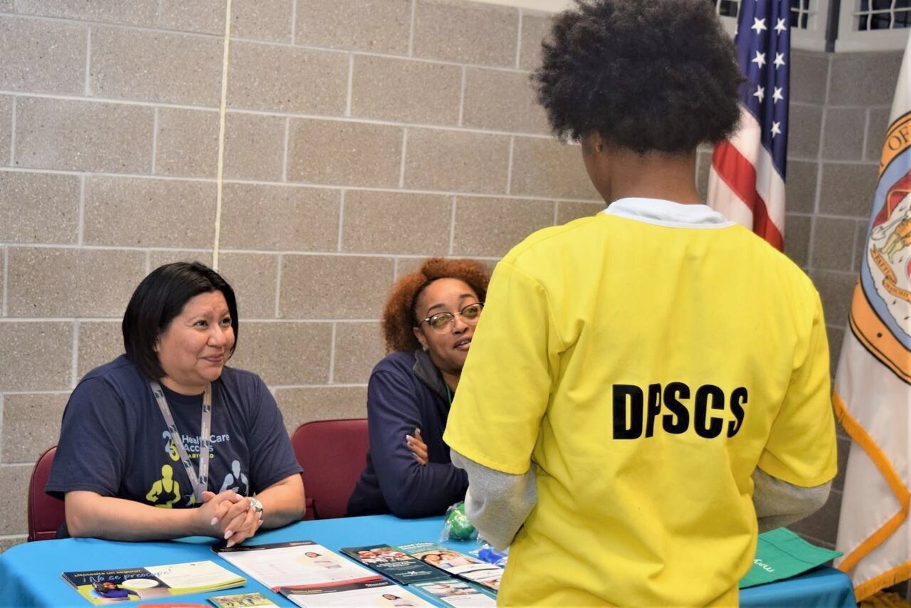 Jessica Delgado, left, and Kezia Tate of HealthCare Access Maryland's enrollment team meet with an incarcerated person about their health care coverage during a community resource fair held in December at a state-run youth detention center.
