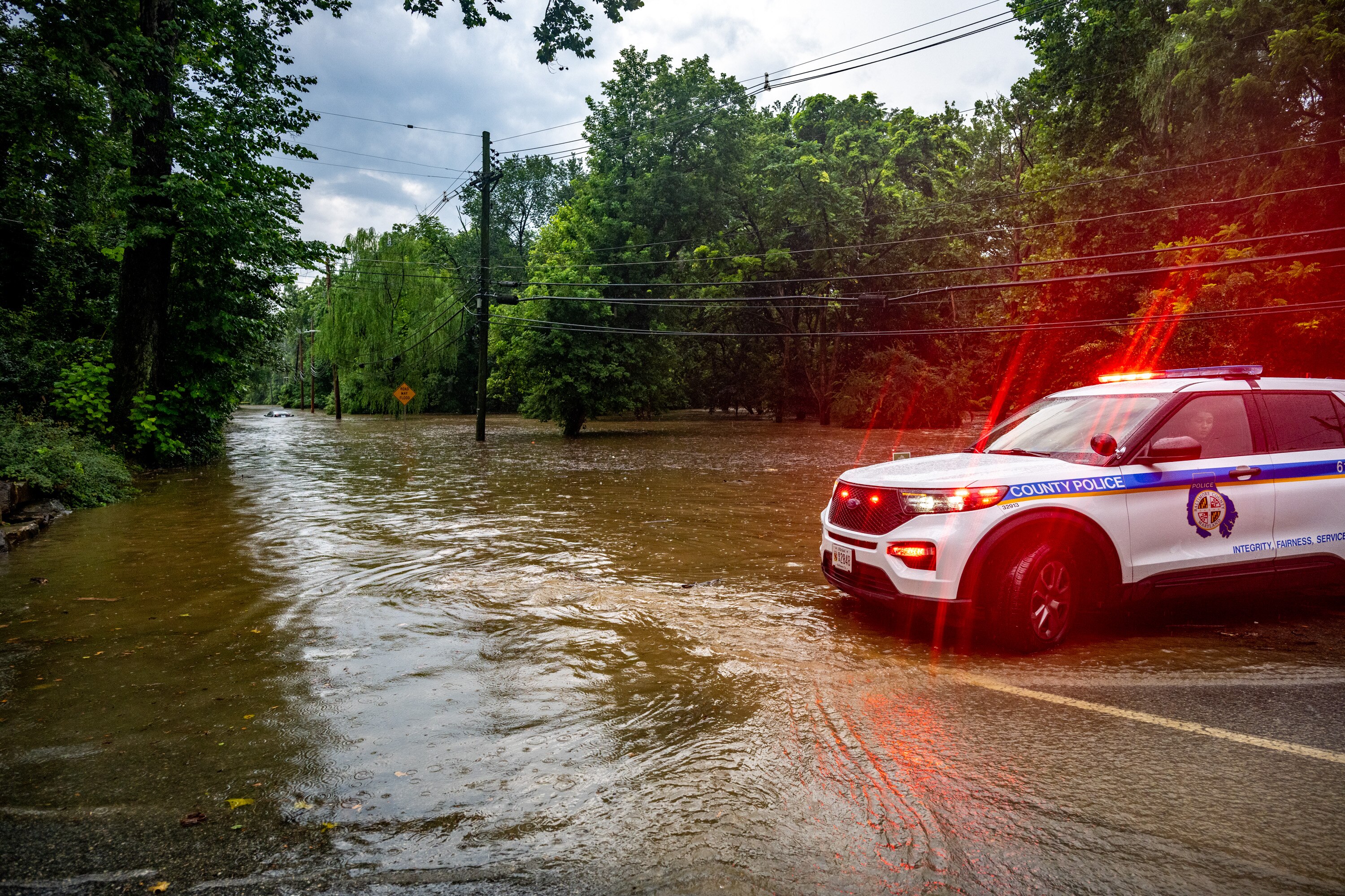 A Baltimore County Police cruiser blocks Ruxton Road where Roland Run spilled over its banks during the afternoon thunderstorms that moved through the region Thursday. 