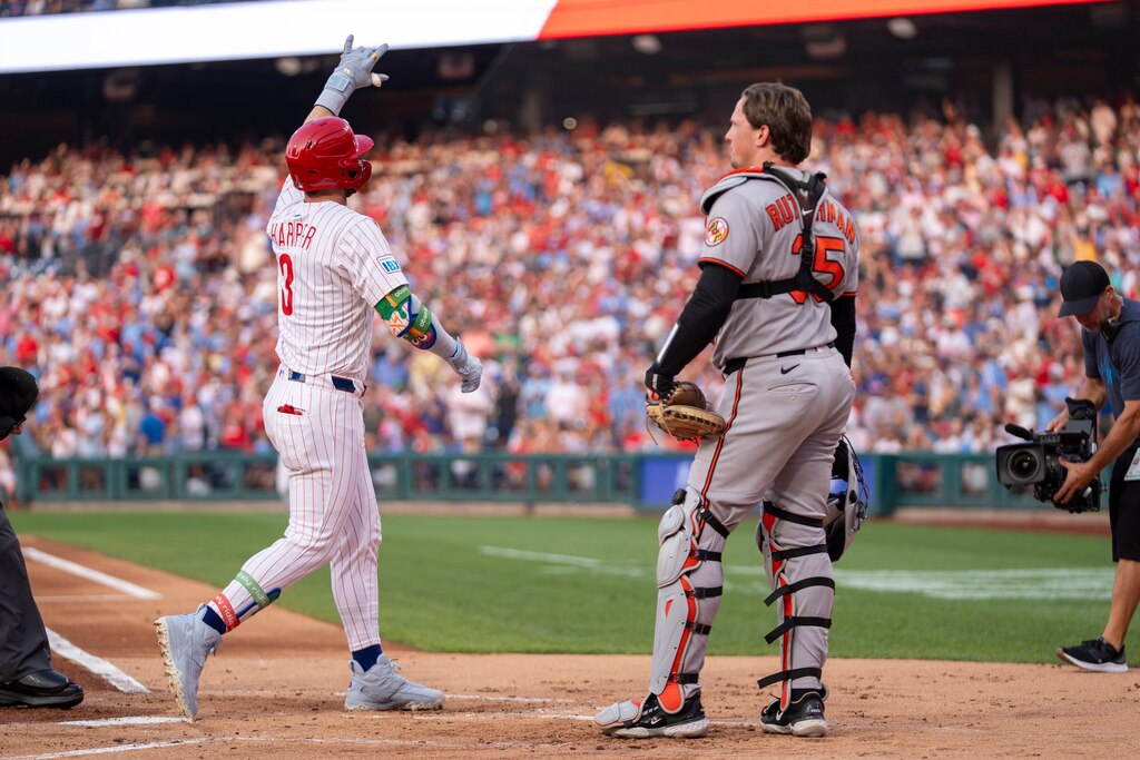 Philadelphia Phillies' Bryce Harper, left, reacts after his home run as Baltimore Orioles catcher Adley Rutschman, center right, looks on.