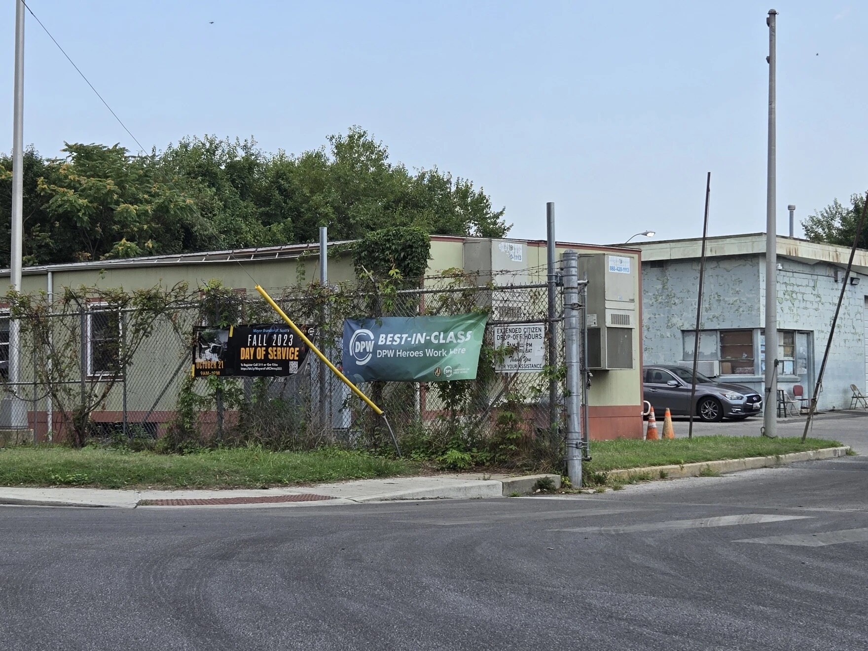 A trailer sits behind a fence covered in vies, with an old, painted brick building in the background.