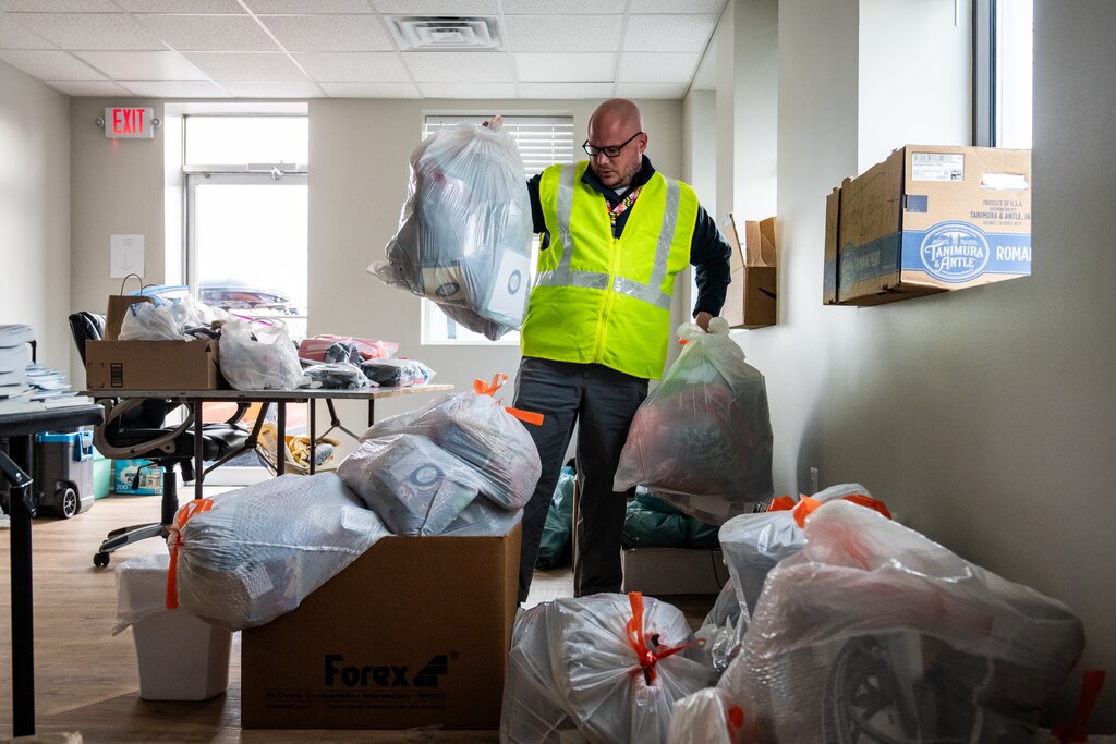 Rev. Joshua Messick picks up two white trash bags full of holiday care packages among a pile of many in the Baltimore International Seafarers’ Center's office.