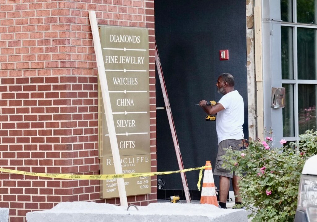 A man works on fixing the front window of Radcliffe Jewelers after a vehicle drove through the window in the early morning hours of August 16, 2023.
