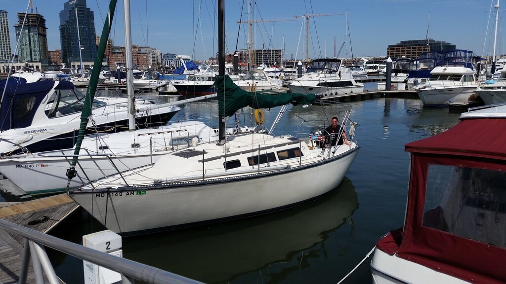 A white sailboat is seen in the middle of the photo with its sails down. Patrick Campbell is seated at the back of the boat.