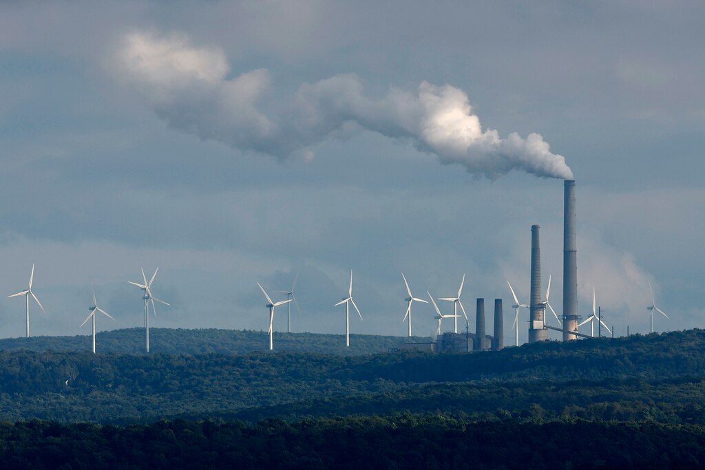 MOUNT STORM, WEST VIRGINIA - AUGUST 22: Turbines from the Mount Storm Wind Farm stand in the distance behind the Dominion Mount Storm power station August 22, 2022 in Mount Storm, West Virginia. The wind farm includes 132 2-megawatt Gamesa G80 wind turbines along 12 miles of the Allegheny Front.