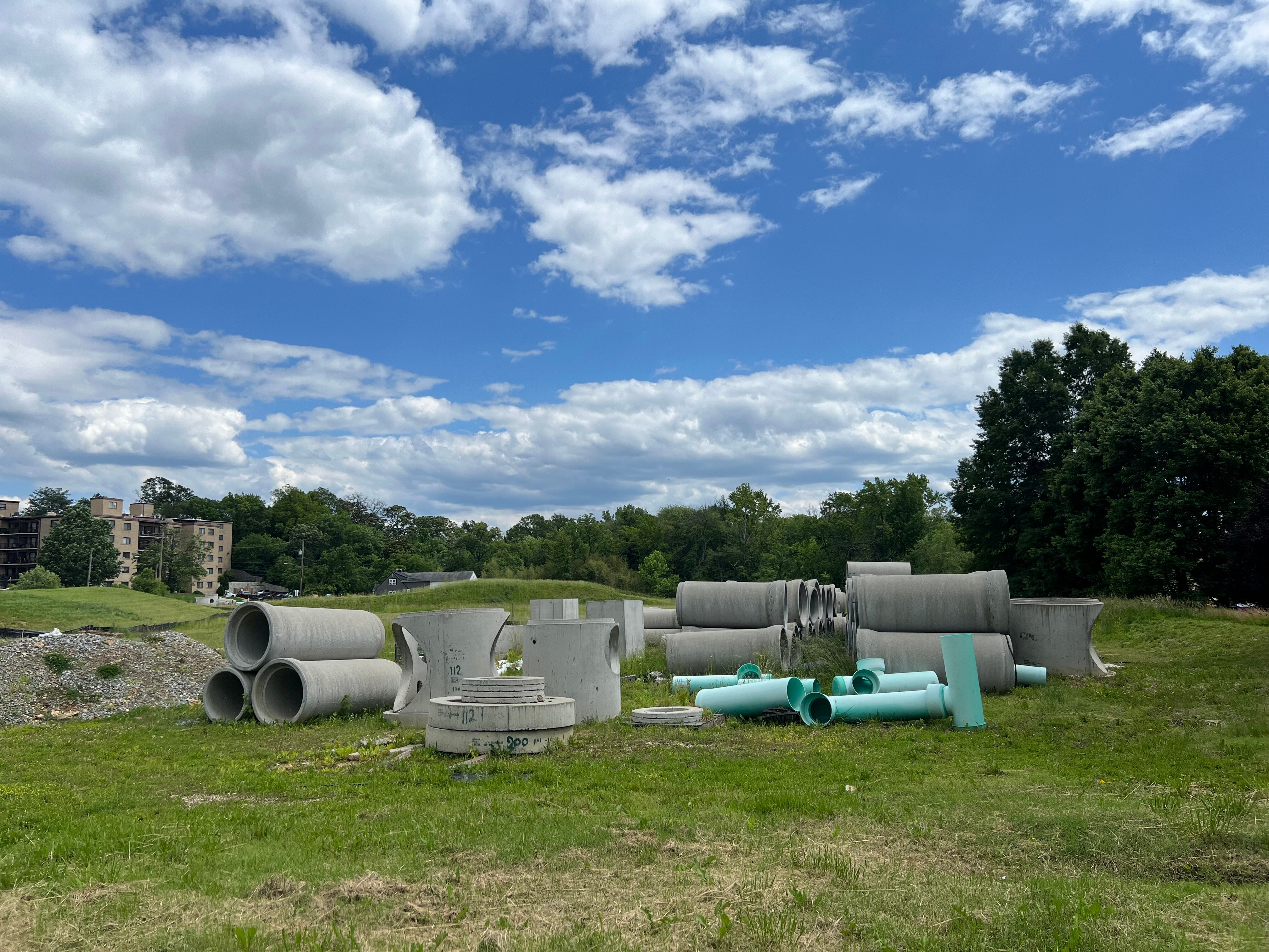 Big concrete pipes sit on on a grass-covered lot.